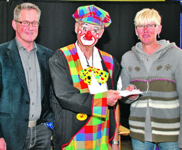 Clown Charly, alias Karl Dimmers, übergibt den Umschlag mit den Spendengeldern an Anja Werning, Vorsitzende der Hattinger Tafel. Über den Besuch freut sich auch Schulleiter Bernd Leven (li.). Foto: Kamphorst