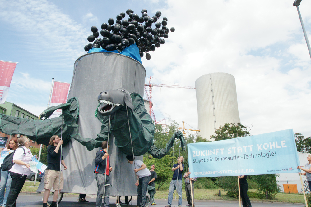 Der Kohlosaurus bläst schwarze CO2-Luftballons in den Himmel.