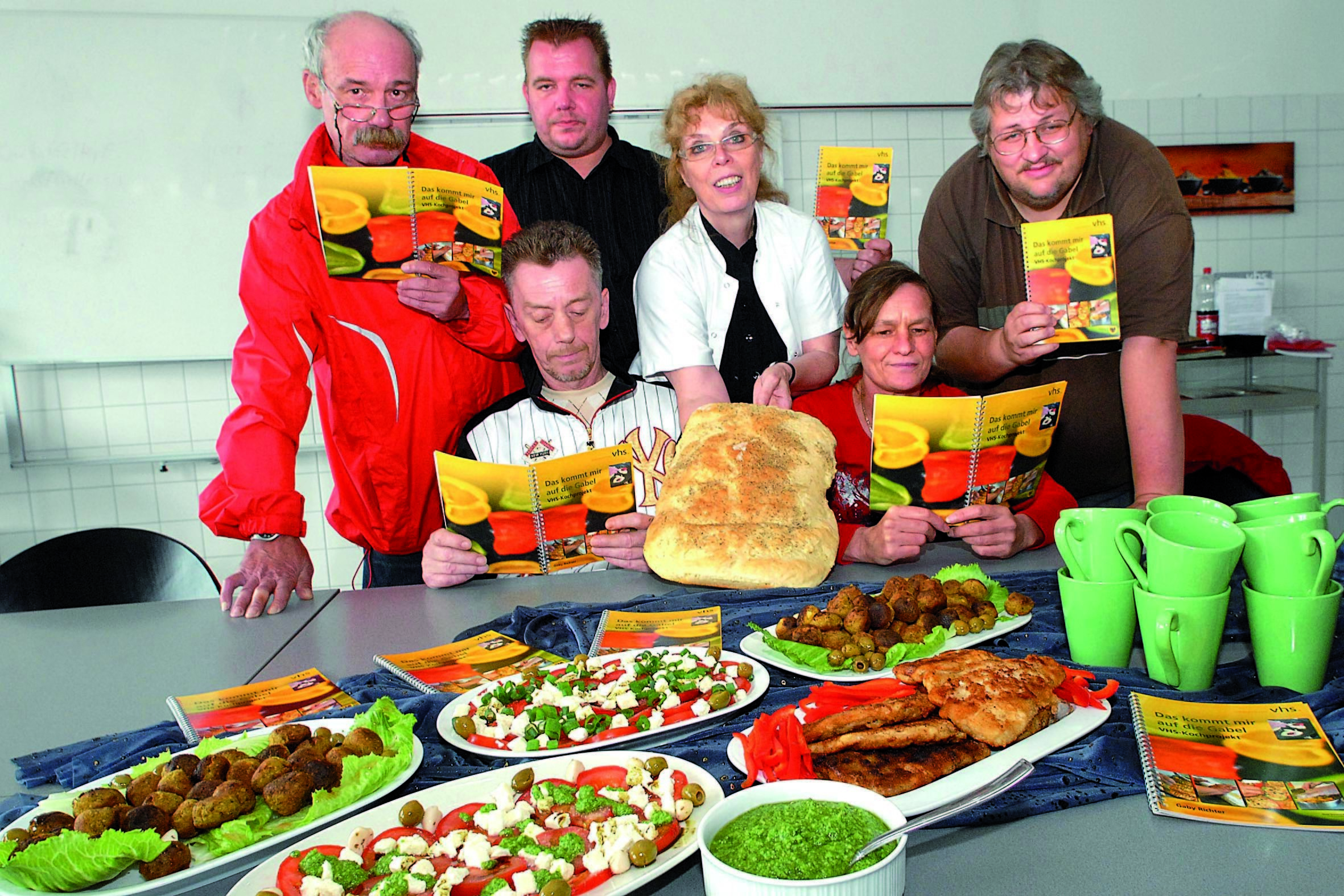 Currycouscous, Tofubällchen, Caprese mit Kürbiskernöl und Pesto-Kanapees sind einige der leckeren Gerichte, deren Rezepte VHS-Kursleiterin Gabi Richter (M.) , Dozentin mit Teilnehmern in einem Kochbuch zusammengestellt hat. Foto: Schmitz