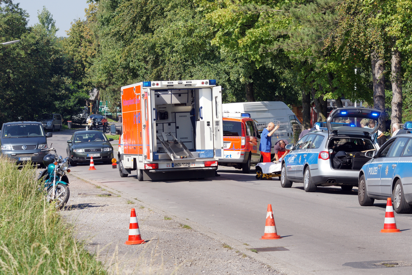 Die Straße ist gesperrt, die Retter kümmern sich um das verletzte Kind. Links im Bild ist das Motorrad zu sehen.