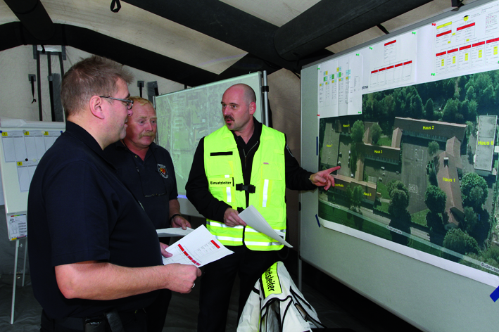 Olaf Weischenberg (r.), Leiter der hauptamtlichen Wache in Unna, erklärt den Leitern der Feuerwehren Holzwickede und Fröndenberg, Jürgen Luhmann (l.) und Jörg Sommer (M.) den Lageplan des Übungsgeländes.