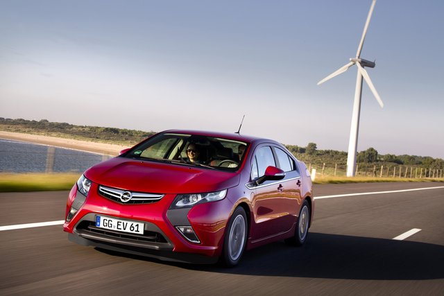 Der Ampera vor einer Windanlage.