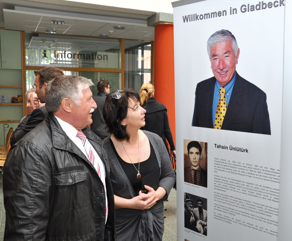 Walter Hüßhoff, Initiator der Wanderausstellung „Hände“, und Unternehmerin Hülya Haack-Yol vor dem Lebenslauf ihres Vaters Tahsin Ünlütürk, der im Februar 1964 nach Gladbeck kam, zunächst als Bergmann, dann als Dolmetscher arbeitete und später Arbeitnehmervertreter wurde.