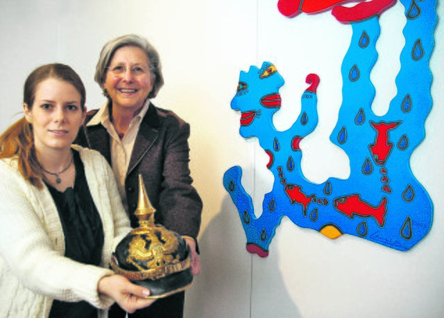 Kuratorin Linda Oberste-Beulmann und die erste Vorsitzende des Fördervereins, Annette Kleyboldt, präsentieren eine preußische Offiziers-Pickelhaube (um 1900) vor dem Bild „Fisherman’s Friend“ von Christoph Mandera (2005).
WB-Foto: Detlef Erler