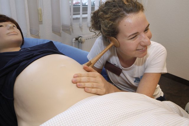 Stipendiatin Sandra Humm, hsg-Studentin der Hebammenkunde, zeigt, wie das Abhören der kindlichen Herztöne mit einem Hörrohr an einem Simulator eingeübt wird.
