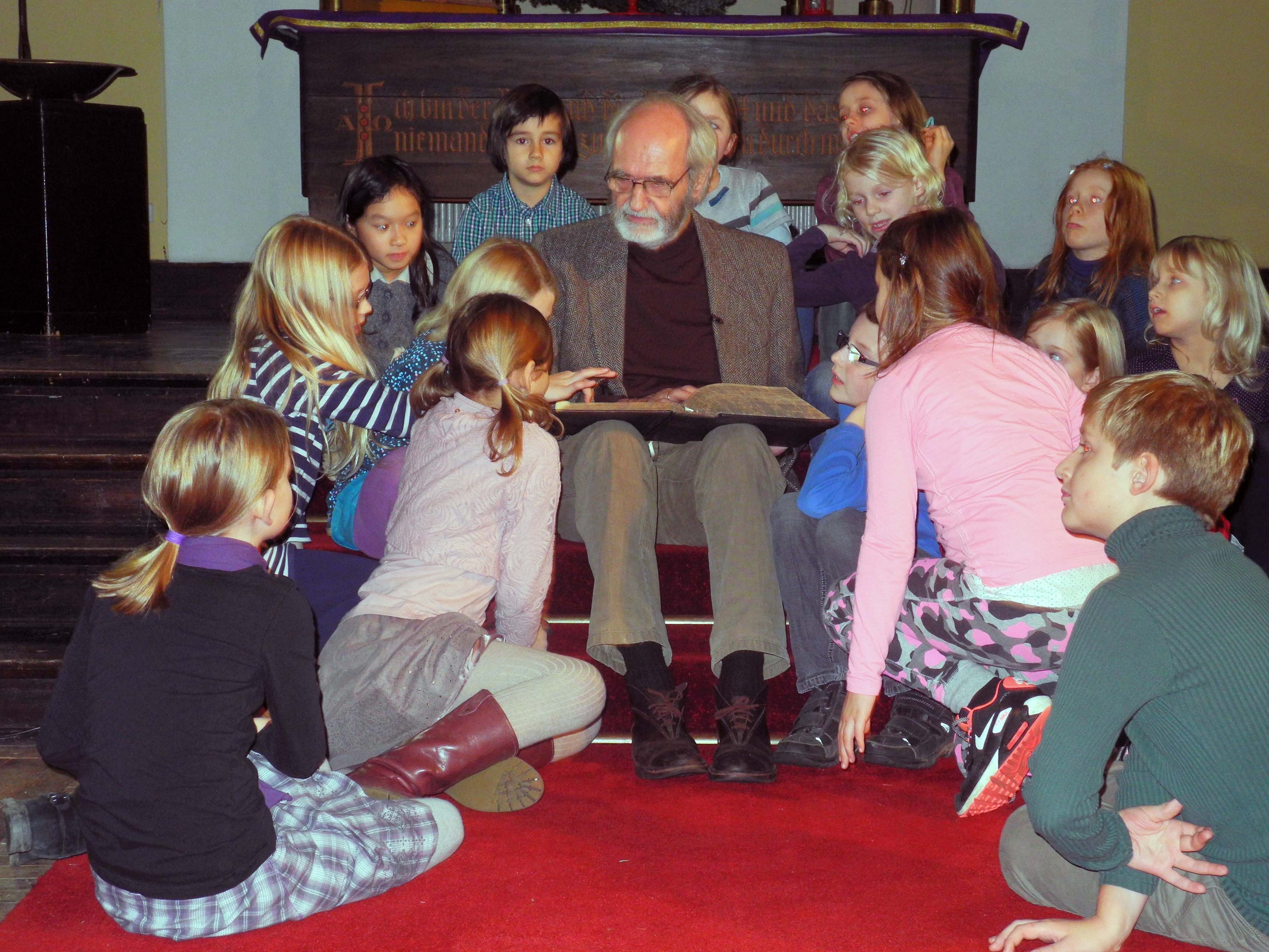 Pfarrer i.R. Hans Adolf Rosenboom liest den Krippenspielkindern vor dem Altar aus der Weihnachtsgeschichte vor.