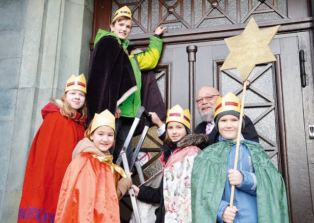 Die Sternsinger bringen gemeinsam mit dem stellvertretenden Bürgermeister Heinz-Peter Schreven die Buchstaben C, M und B über der Tür des Heiligenhauser Rathauses an.