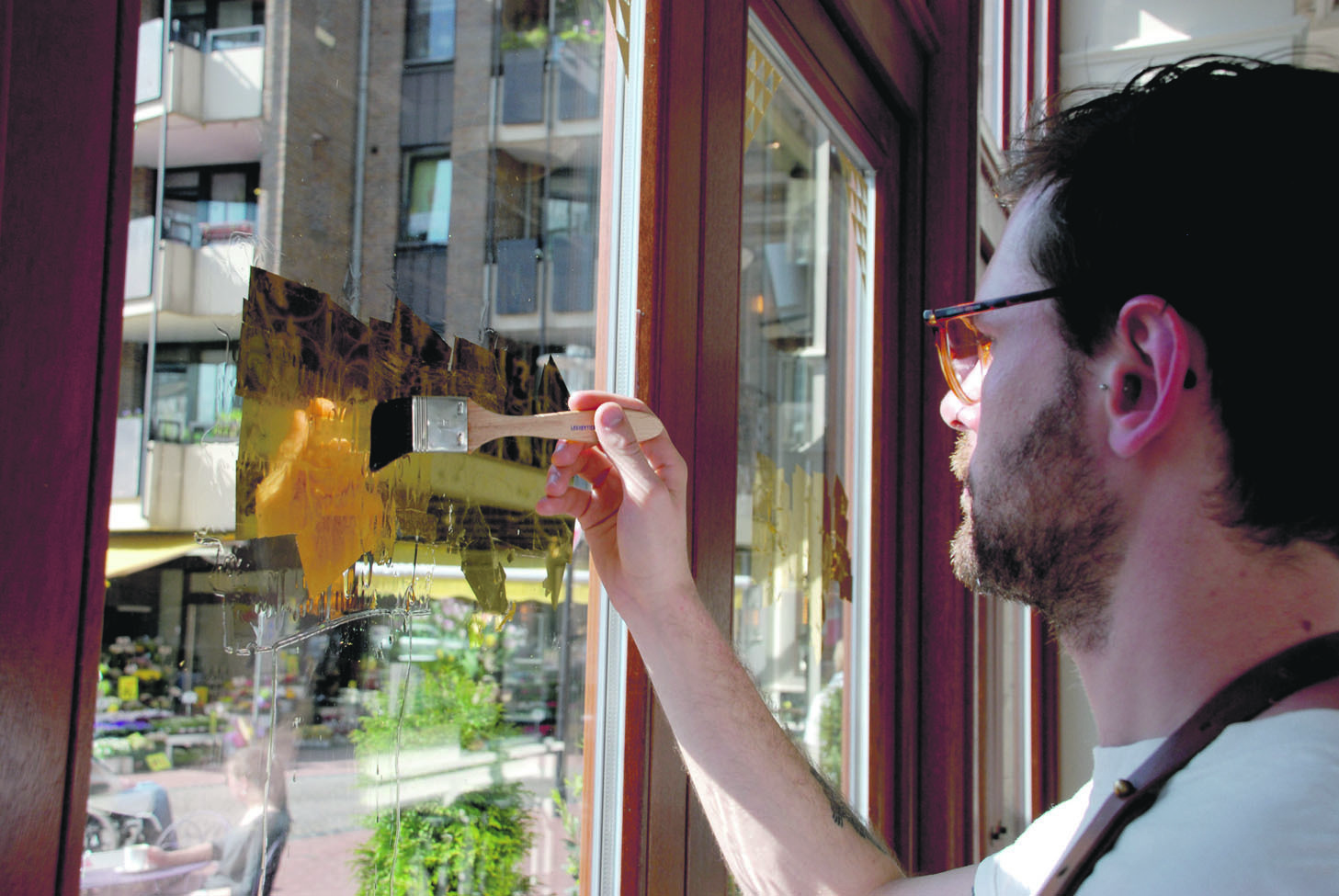 Ganz vorsichtig trägt Ged Palmer das Gold Blatt für Blatt auf die Scheibe auf. Später entstehen daraus die Ziffern "1910" - der Name der neuen Brasserie.