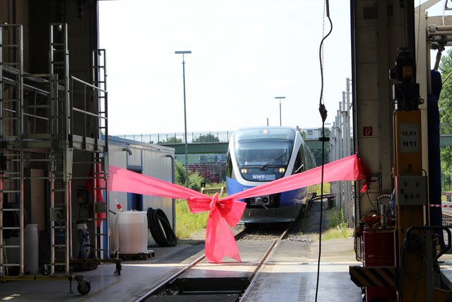 Symbolische Einweihung der ausgebauten Werkstatt: Ein Zug der NordWestBahn durchfährt ein rotes Band im Eingang zur Werkstatthalle.