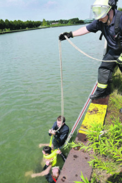 Erst ans sichere Ufer und dann mit der Rettungsschlinge an der hohen Spundwand hochgezogen wird ein Verunglückter bei einer Wasserrettungsübung am Hafen.