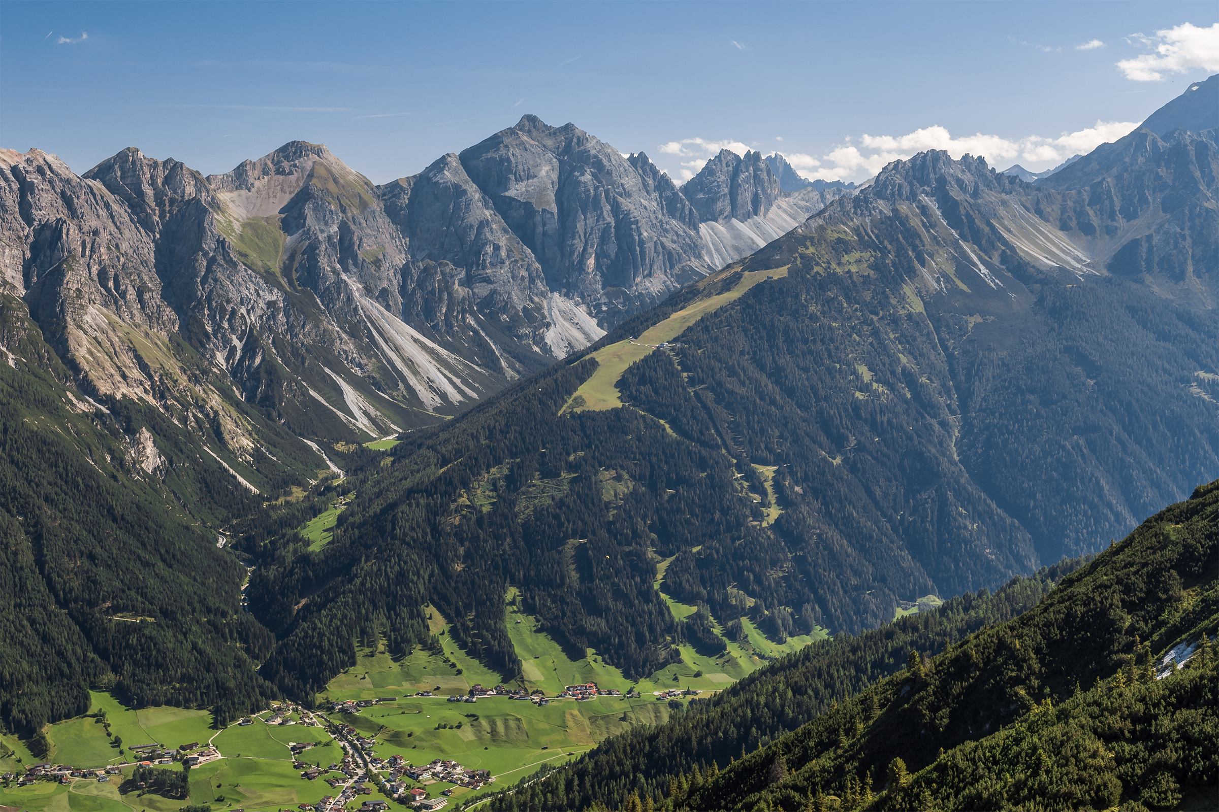 Dieses Bild gehört nicht zur hier erläuterten Wanderung, zeigt aber das Gebiet sehr gut: Der bewaldete Berg in der Bildmitte ist der Elfer. Man erkennt die Grasflächen des Skigebietes und als dünnen Strich die dahin führende Seilbahn. Oben mündet der Elfer dann in den Elferspitzen. Hinter dem Elfer liegt das Pinnistal, dass im Bild unten dann ins Stubaital mündet.