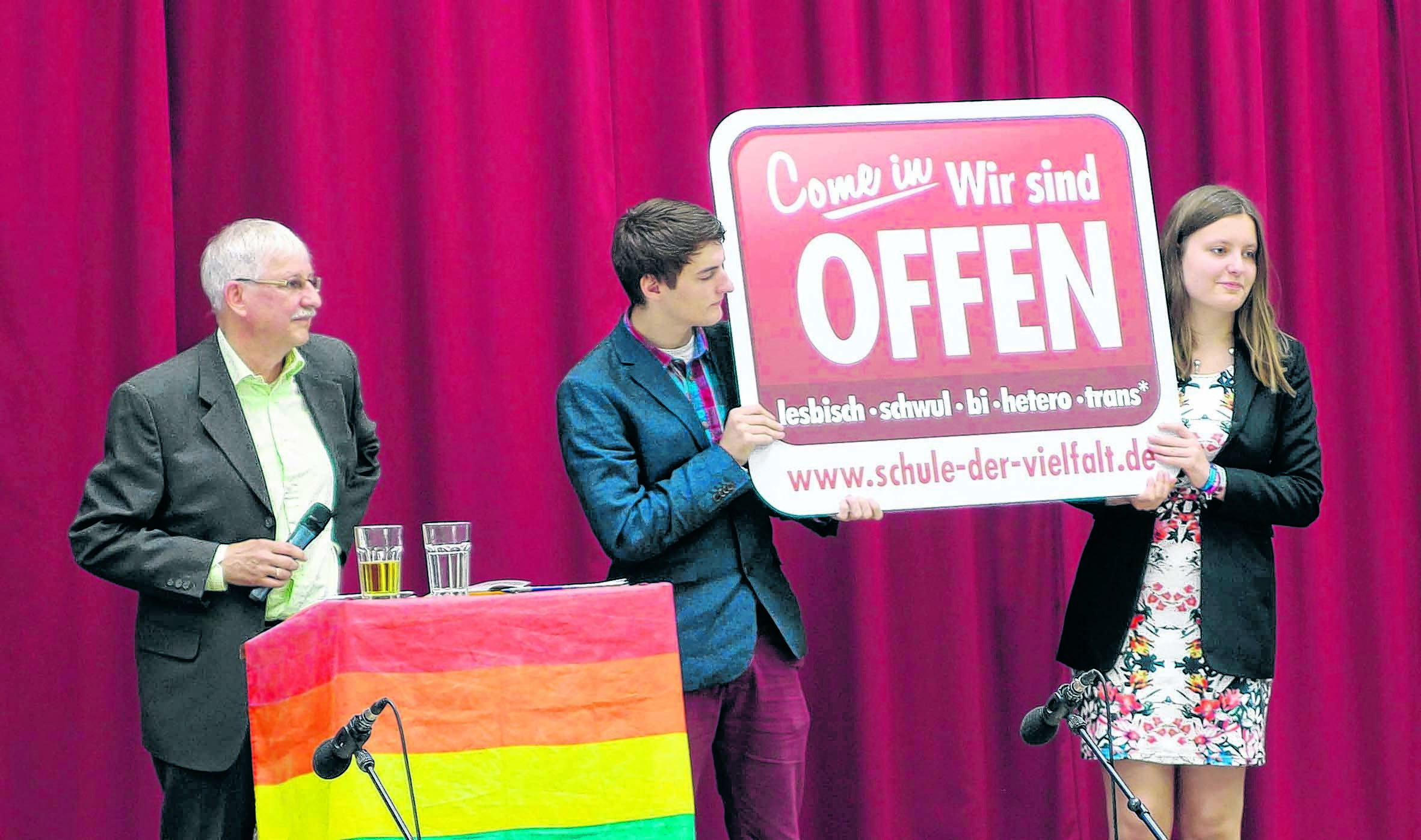 Theo Reidick, stellvertretender Schulleiter, und die Schülersprecher Samuel Höfer und Maja Iwer präsentieren der versammelten Schule das neue Schild für mehr Akzeptanz.