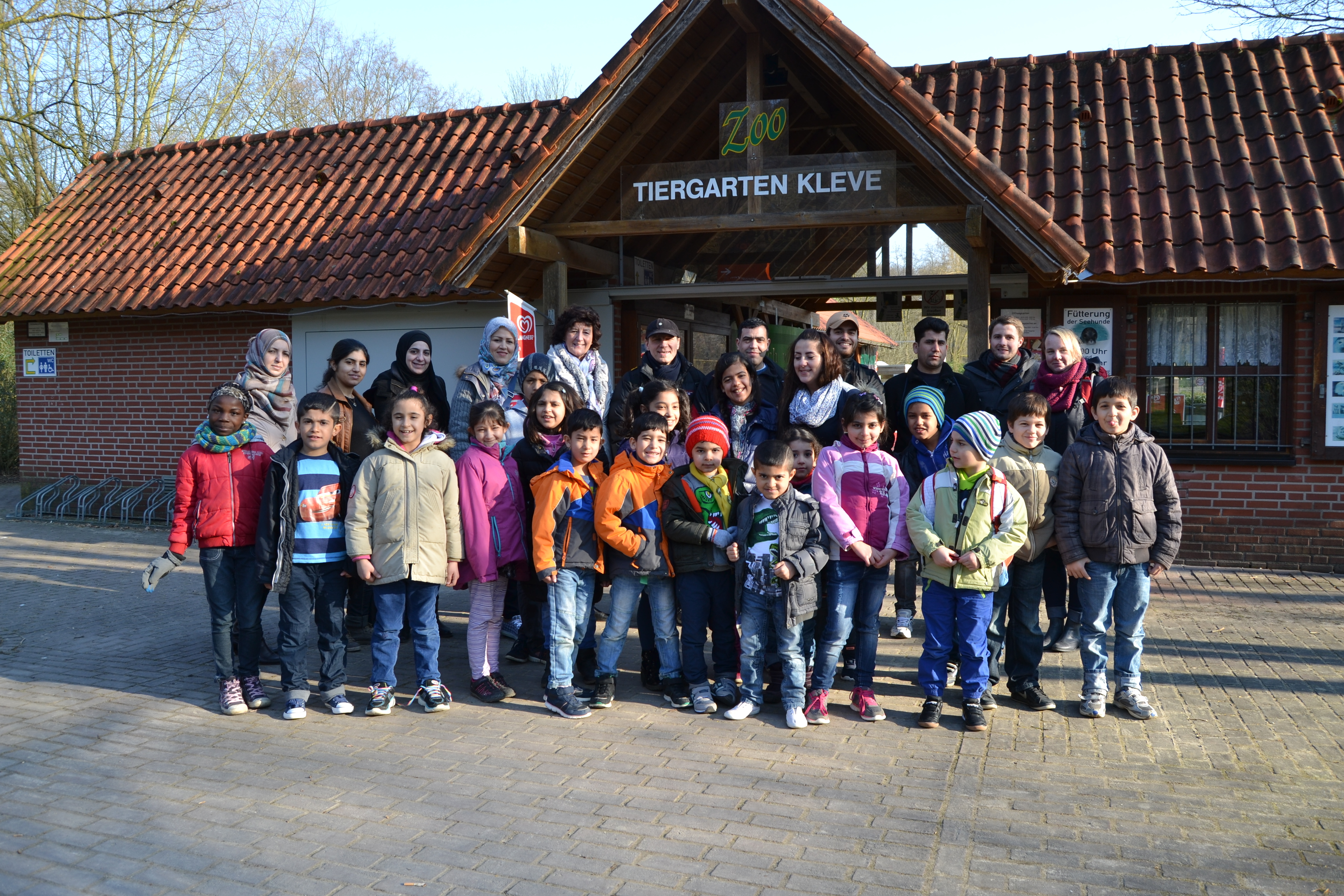 Das Foto zeigt die Schulkinder mit ihrem Lehrer Lukas Bergmann (hinten 2. von rechts) sowie ehrenamtlichen Begleiterinnen und einigen Eltern vor dem Tiergartenbesuch.