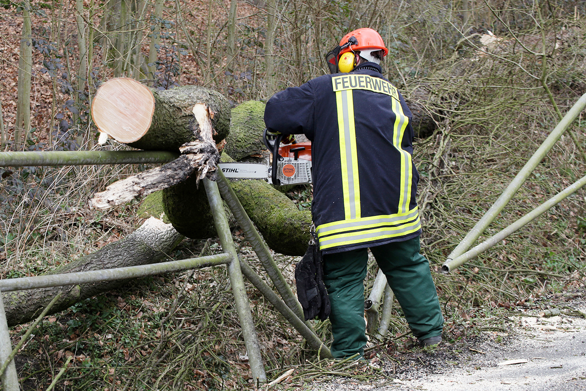 Der Baum zerstörte ein Geländer, eine Feuerwehrfrau schneidet den dicken Stamm in Stücke.
