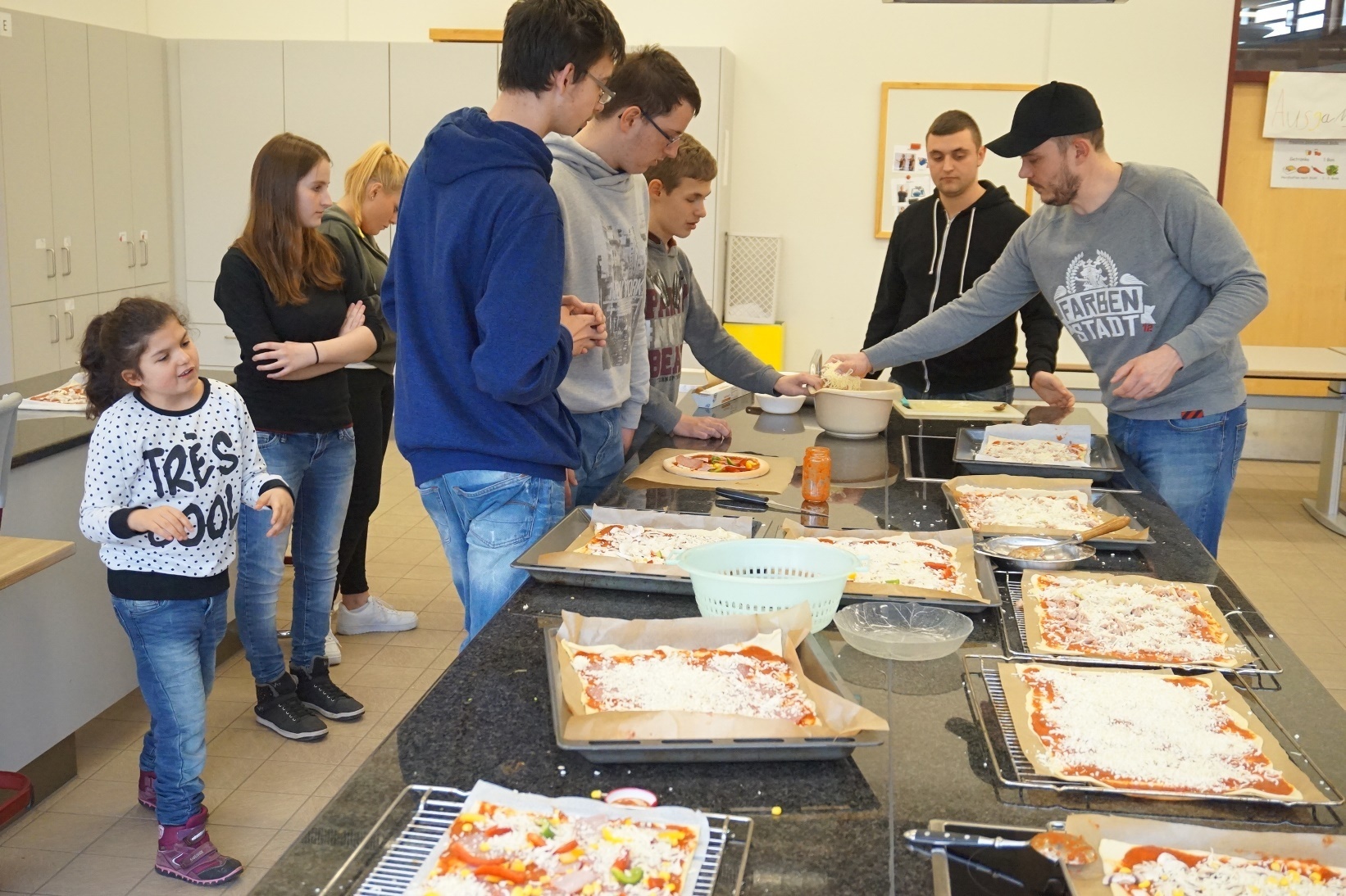 Unter Anleitung von Markus Jordan (rechts) wurden die Pizzen belegt, zum Schluss wurde geriebener Käse drübergestreut.