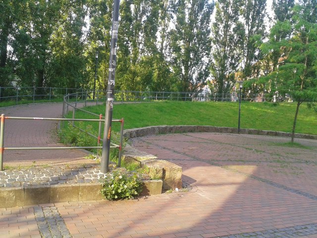 Ursprünglichenhn hatten sich die Stadtplaner bei der Sanierung des Altenessener Ortskern vorgestellt, dass hier z.B. ein Eiscafe für Belebung und sozaile Kontrolle sorgen könnte. Jetzt gibt es leider nur Gras - keine Bänke, keine abwechslungsreiche Bepflanzung, kein einziges Spielgerät für Kinder. Kein Wunder, dass man dort leichter auf leere Bierflaschen unterschiedlicher Marken treffen kann.