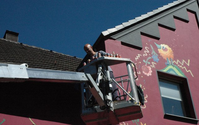 Für Gabor Doleviczenyi geht es mit dem Hubwagen hinauf bis an den Giebel. Dort sprüht er zum Abschluss der Arbeiten einige letzte verbindende Elemente.