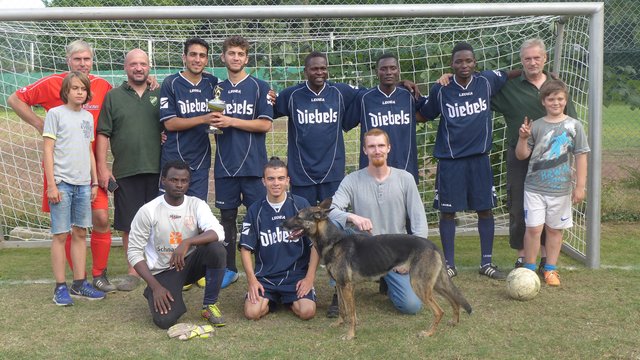 Eine starke Mannschaft und ihre Freunde: (von links): Torsten Otting, Noah Khalaf, Siegfried Jahr, Abdal Houssam, Mohammed, David, Hassan, Michael Weber, Felix Jahr, Elias, Hamid, Leopold Nienhaus und seine Schäferhündin Mia nach dem erfolgreichen Turnier beim TBD Speldorf, das sie als Drittplatzierte mit einem Pokal abschließen konnten. (Foto Emons)