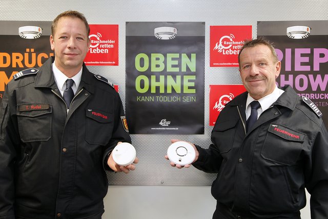 Feuerwehr-Chef Rainer Ashoff (r.) und Thorsten Rudel, Sachgebietsleiter für den Brandschutz, werben mit Unterstützung frecher Plakate für die so wichtigen Rauchmelder