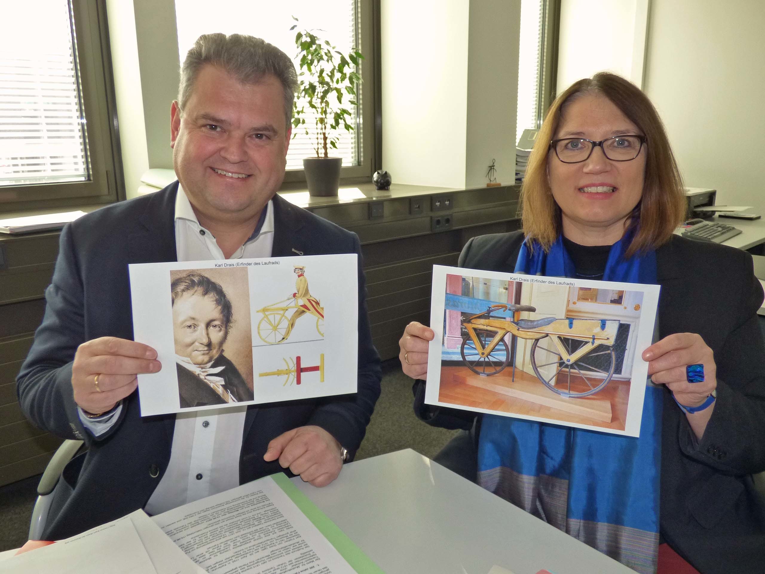 Michael Blaess, Fahrradbeauftragter und Ulrike Westkamp, Bürgermeisterin, präsentieren den Erfinder Karl Drais (li) und sein Laufrad (re)