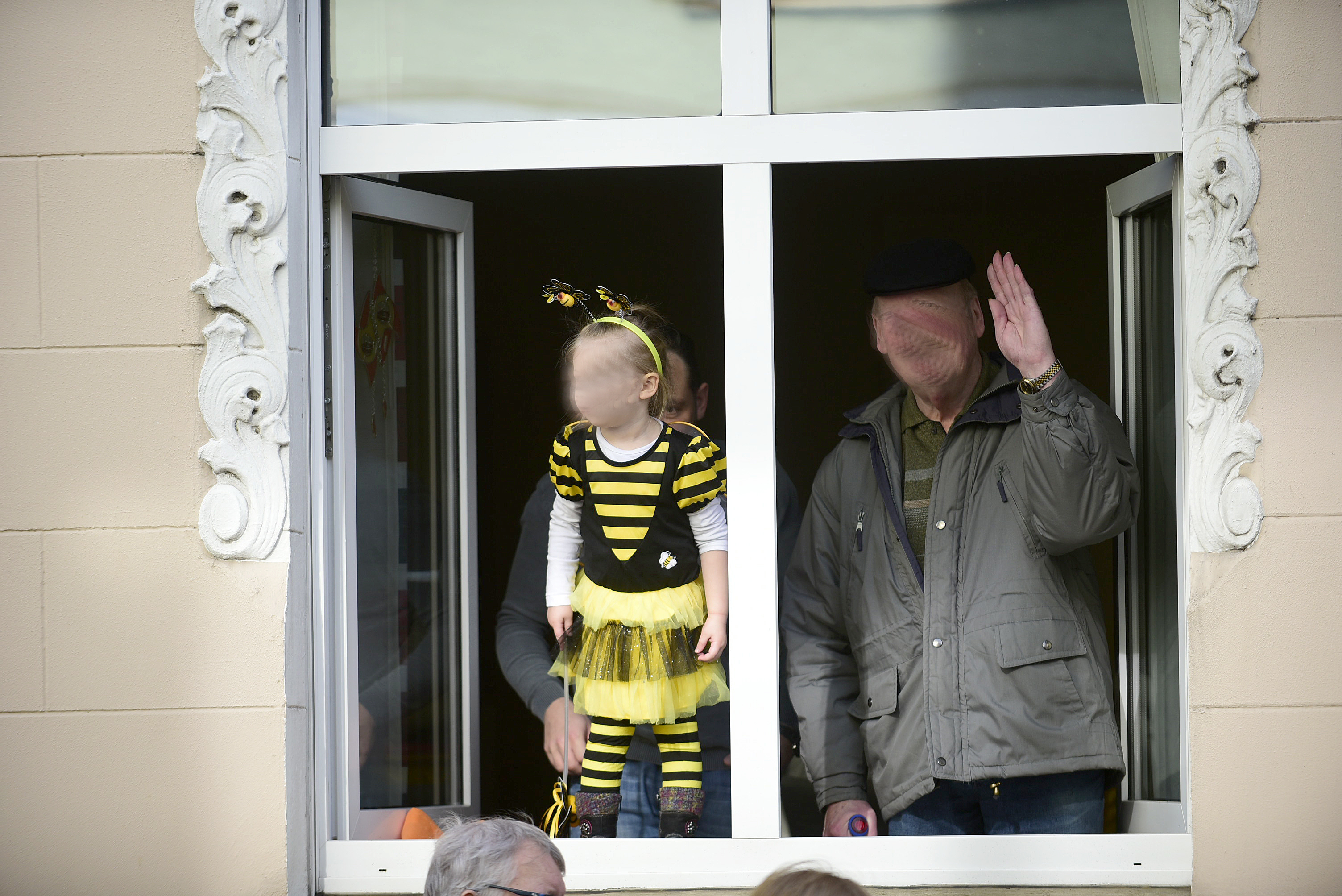 Papa hält die Kleine von hinten an den Beinen fest und Opa steht daneben und winkt den Jecken zu. Foto: Eberhard Kamm