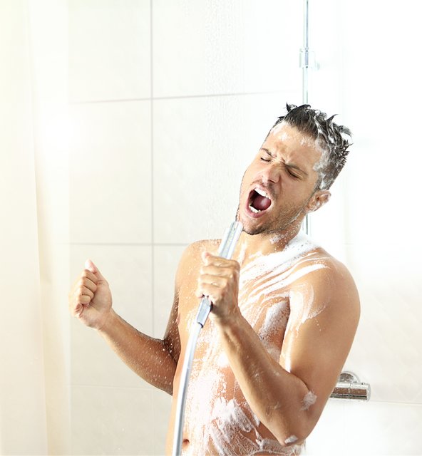 Early 30's caucasian man singing under morning shower. He's using shower head as microphone. He''s covered with soap and shampoo. Eyes closed, front view.