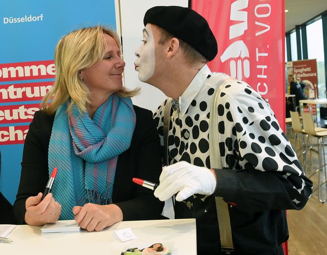 Maike Münster am Stand der Handwerkskammer Düsseldorf freut sich über den Besuch von Pantomime Paul vom Ensemble Finesse.