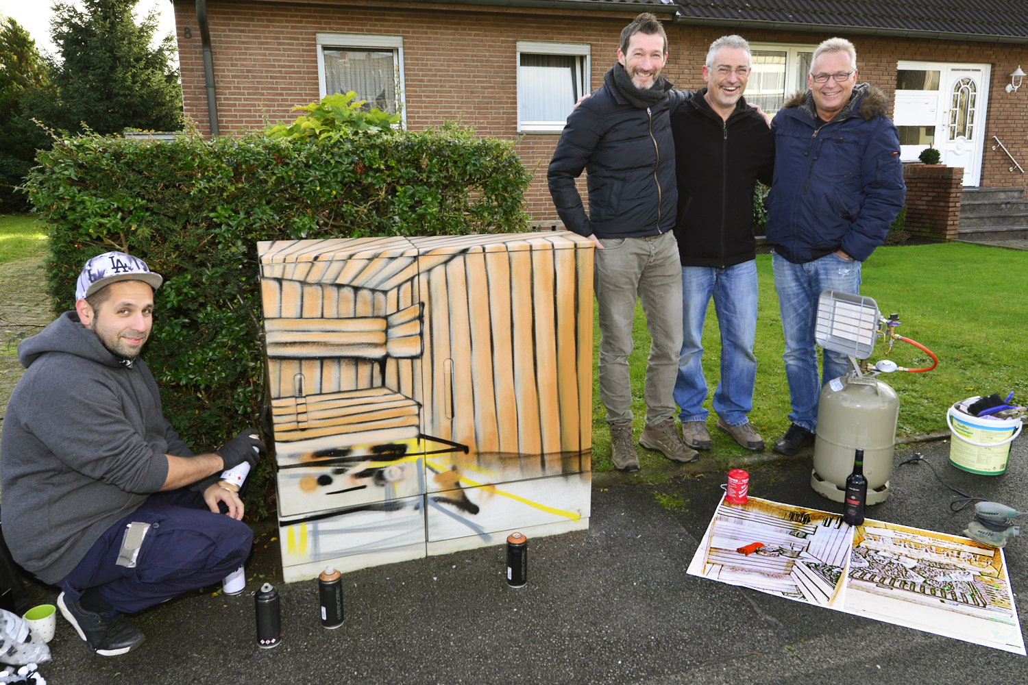 Mauricio Bet (links) im Einsatz: Unter den Augen von Christian Kuhlmann, Andreas Knittel und Rainer Rosier (stehend von links) verhalf der Graffiti-Künstler dem Stromkasten an der Lötzener Straße in Rentfort zu einem farbenfrohen Sauna-Motiv.