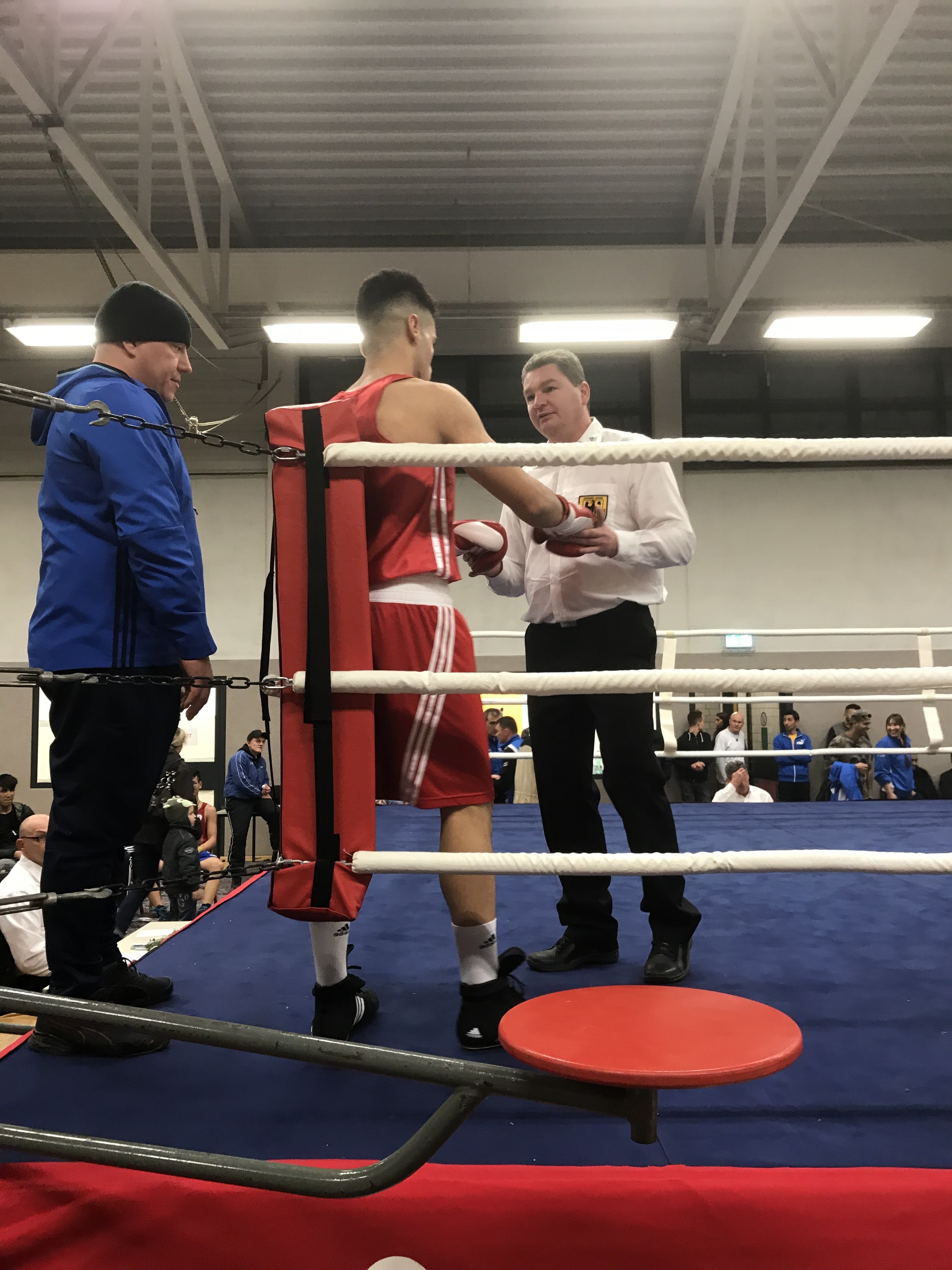 Ringrichter Thorsten Broll überprüft vor dem Kampf die Boxhandschuhe des Kämpfers Malek Alhamwi (DBS 20/50). Der DBS-Trainer Martin Cwiklinski schaut zu.