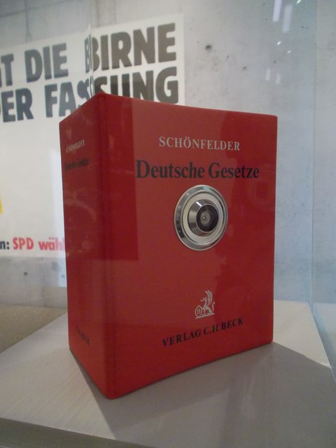 "Der große Lauschangriff" (1996). Das Buch der Deutschen Gesetze mit dem Türspion.