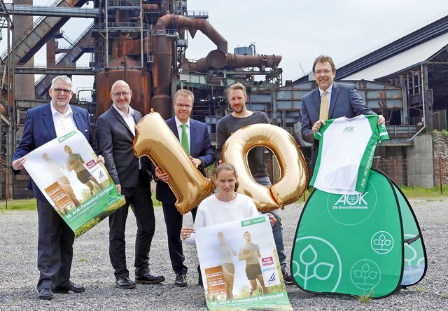 Freuen sich auf den AOK-Geburtstagslauf (v.l.) mit der Zahl „10“: Klaus Holtkamp (Mediaberater Stadt-Anzeiger), Dirk Stürmer (TechnologieZentrumDortmund), Jörg Jockisch (Spezialist Presse Serviceregion AOK), Marcus Hoselmann (Agentur upletics.) sowie Jens Kuschel (Pressesprecher AOK NORDWEST) und knieend Laufbotschafterin Jana Hartmann vor der beeindruckenden Kulisse von Phoenix-West.