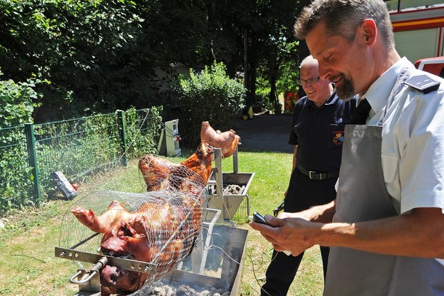 Löschzugführer Frank Tiggemann überprüft die Gartemperatur der Spanferkel. 
Foto: Bangert