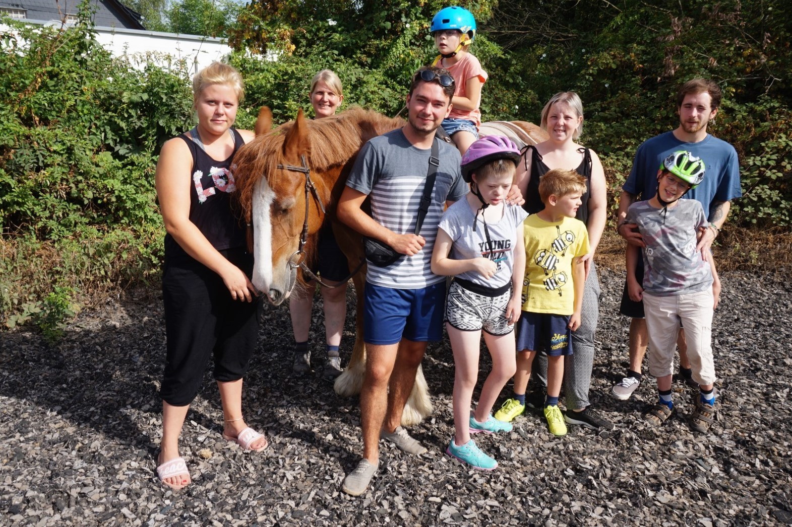 Emilia (10) sitzt als erste auf dem Pferd, umgeben von weiteren Kindern und Helfern, hinter dem Pferd die Reittherapeutin Marion Hupperts.