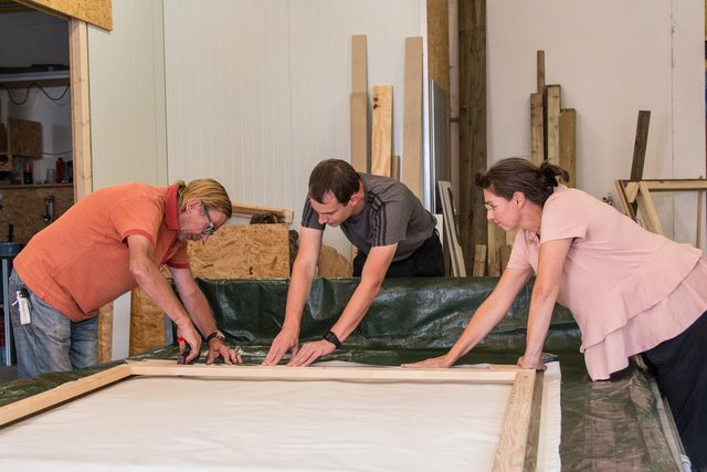 Fredo Ouvrier de Longwy, Mike Feische und Iris Willeke müssen kräftig anfassen, um die Leinwand gespannt zu bekommen.