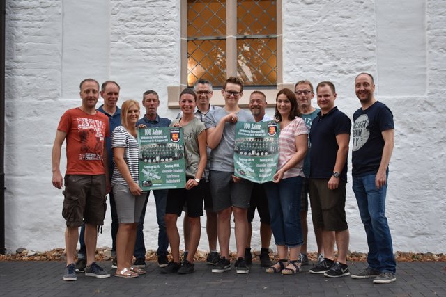 Musiker präsentieren die Plakate zum Jubiläum vor dem Pfarrheim St. Antonius.
