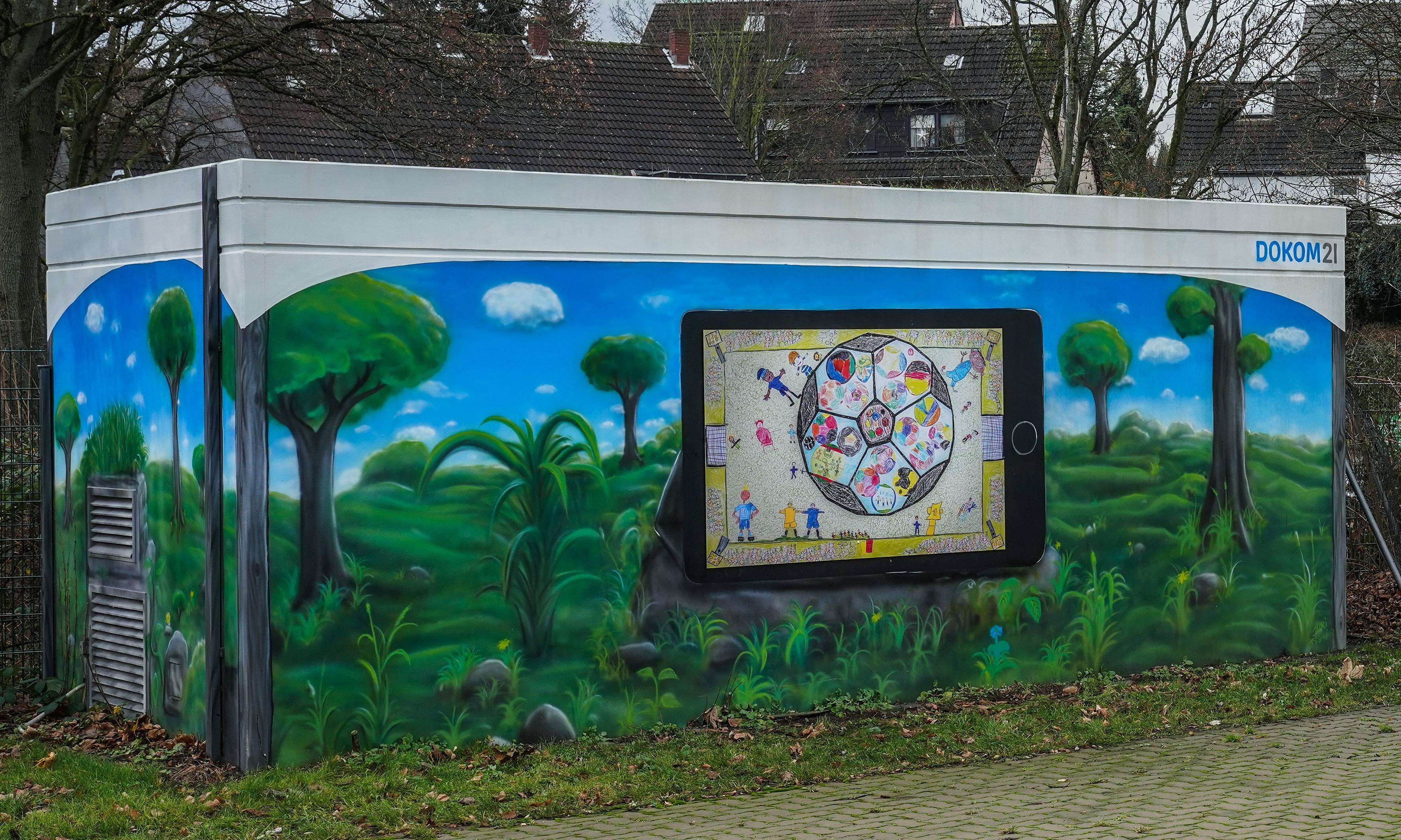 Ein großer, kunterbunter Fußball und junge Kicker auf einem grünen Spielfeld mit Fußballtoren sind jetzt der Hingucker auf der Fassade des DOKOM21 Technikhauses an der Raumerstraße 38.