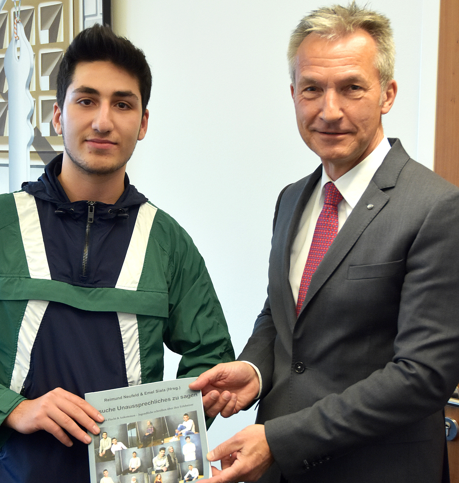 Mohamad Akkourr übergibt Oberbürgermeister Frank Baranowski das Buch mit Erfahrungen von geflüchteten Jugendlichen.