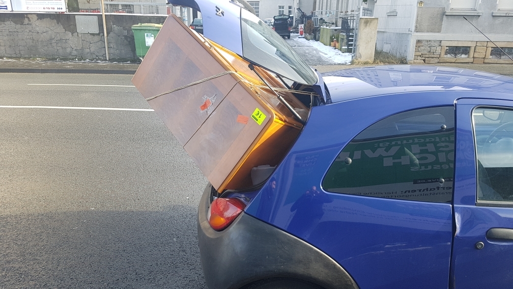 Bei dem Kleinwagen schaut ein Schrank aus dem Kofferraum.