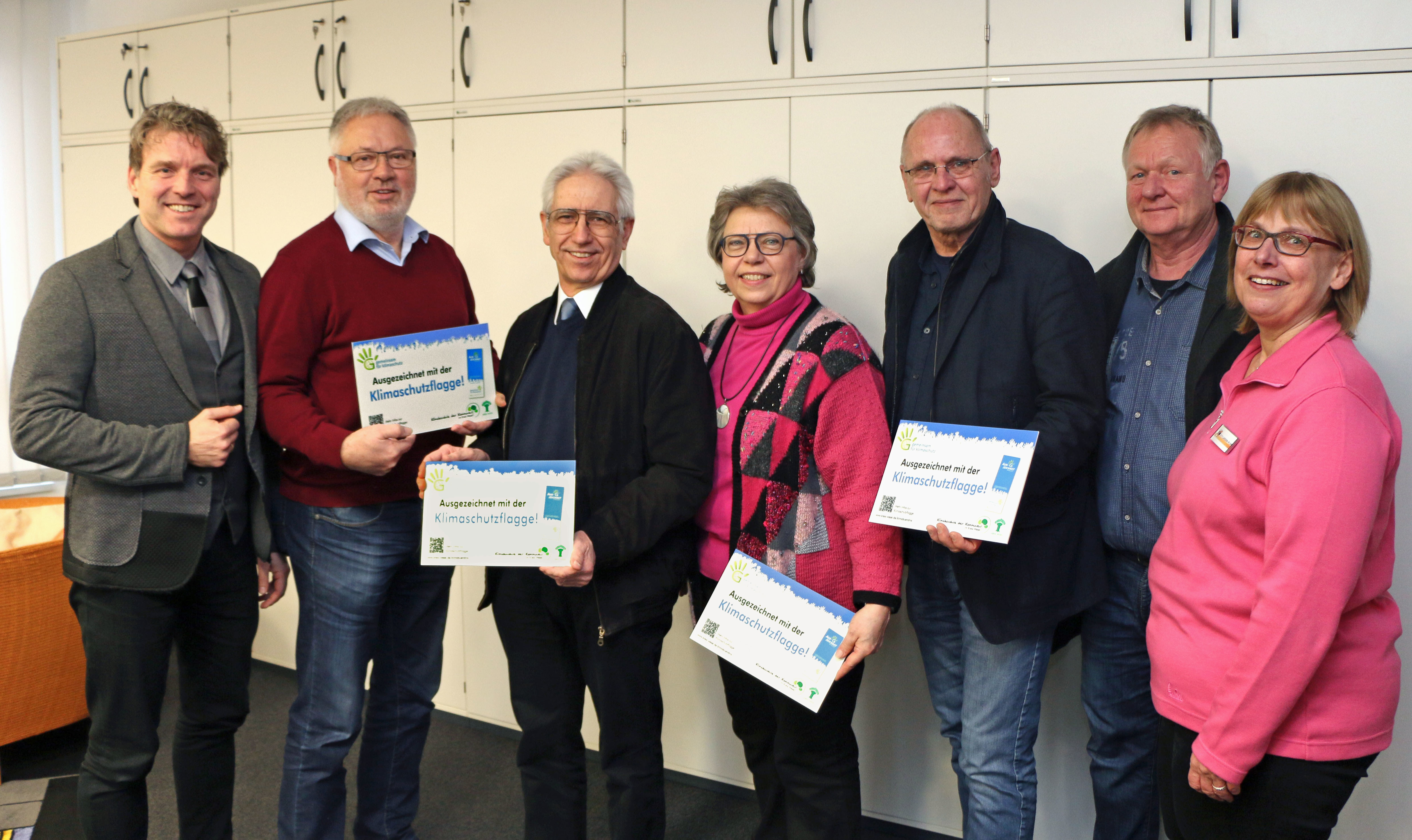 Bürgermeister Christoph Fleischhauer (l.) und Rita Lasson-Ploß (r.) vom Fachdienst Grünflächen und Umwelt überreichten Werner Windbergs (Eick), Jürgen Kienle (Scherpenberg), Heidi Böckle (Hülsdonk), Uwe Neidling und Frank Liebert (Meerbeck) die Schilder für die Klimaschutzflagge.