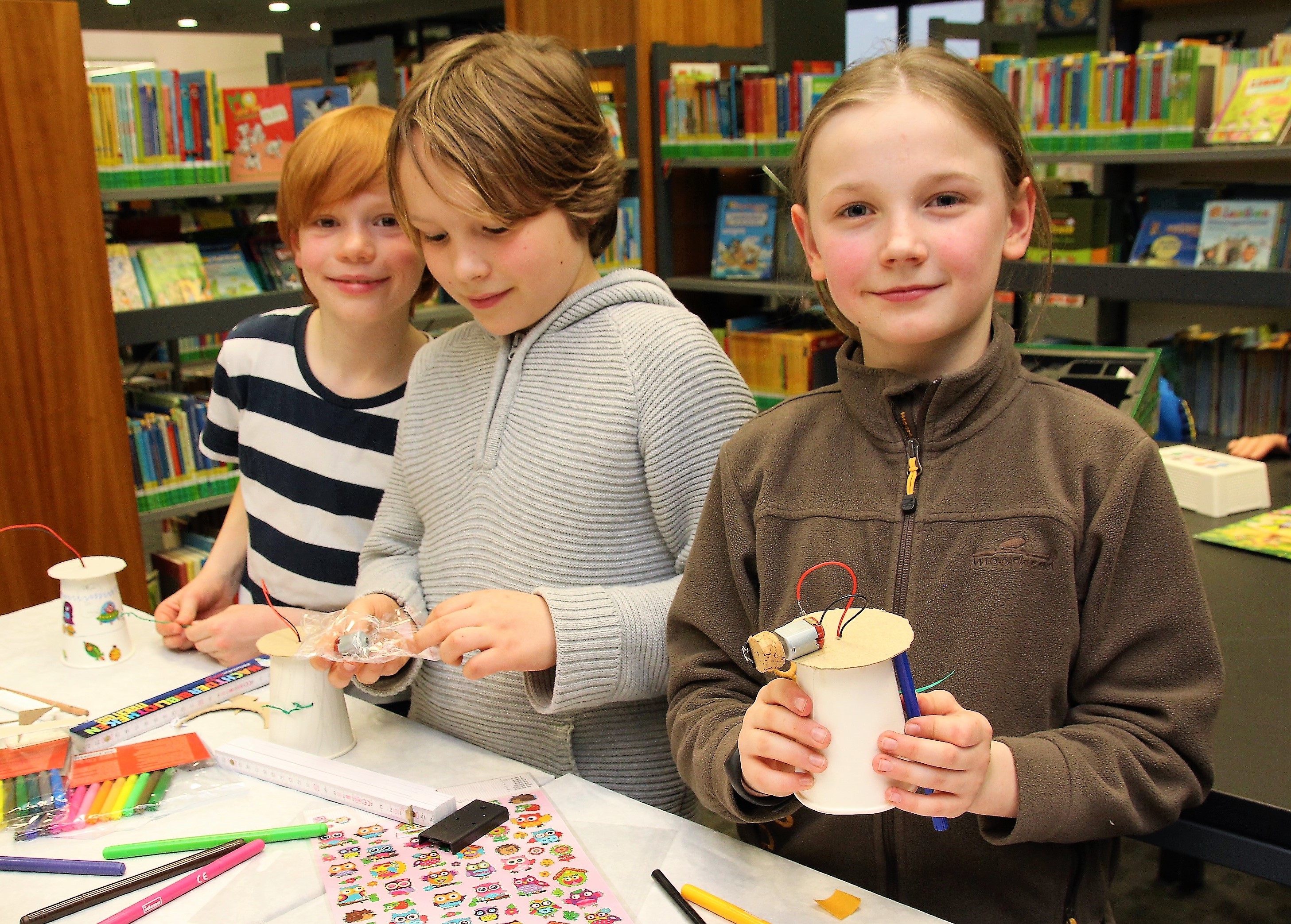 Silas (9), Paul (9) und Kai (9) (v.re.n.li.) sind hier mit Eifer dabei, aus jeweils einem Pappbecher mit Elektromotor einen einfachen Roboter zu bauen, der dann selbstständig Malmuster erzeugt.