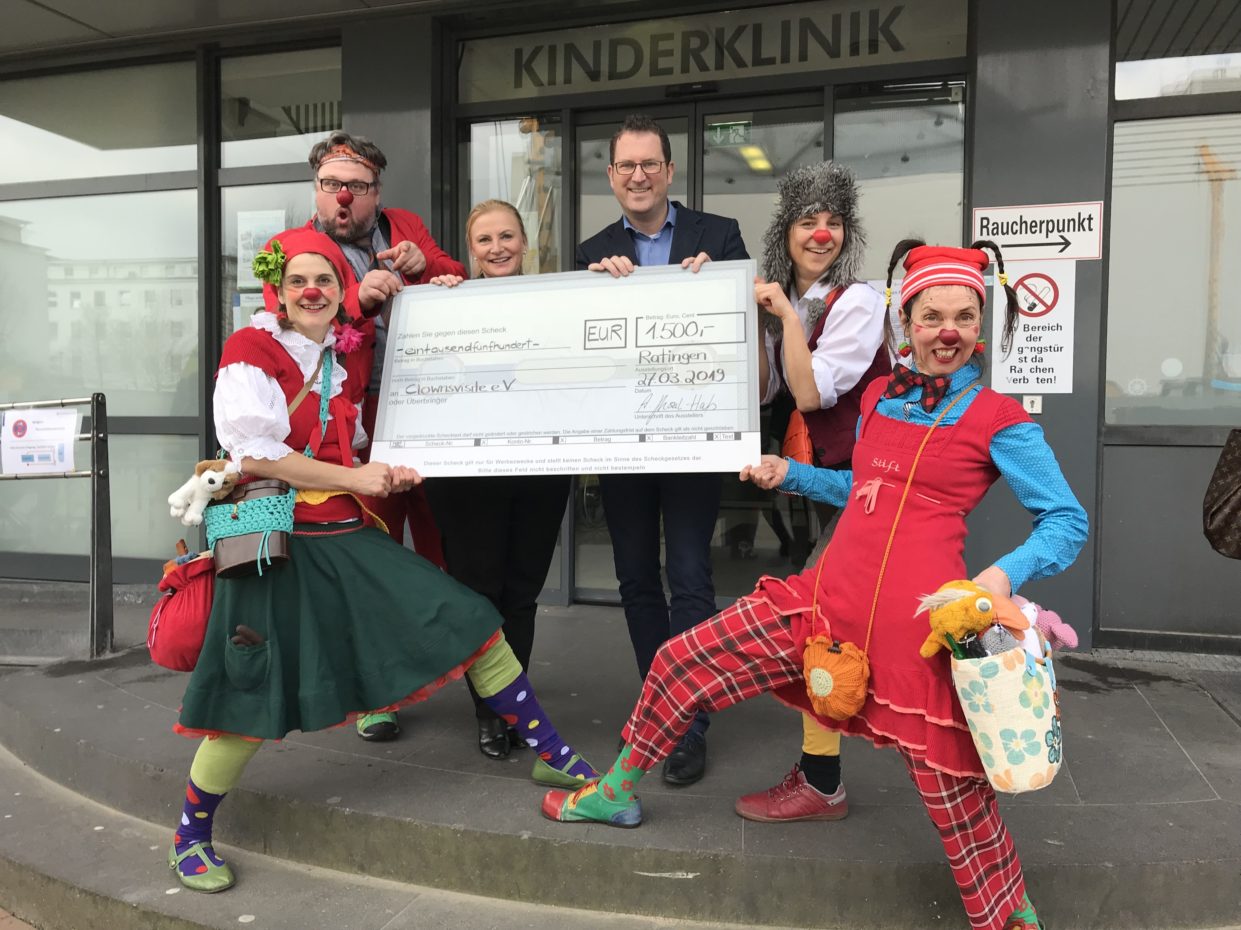 Anita Gluszak-Haefs, Geschäftsführerin Competence Center Telekommunikation, Versicherungen, Travel, Jorit Ness, Geschäftsführer der Stiftung Universitätsmedizin (beide Mitte) und die beiden Teams der Clownsvisiten lachen nicht nur im Angesicht dieser Spende.