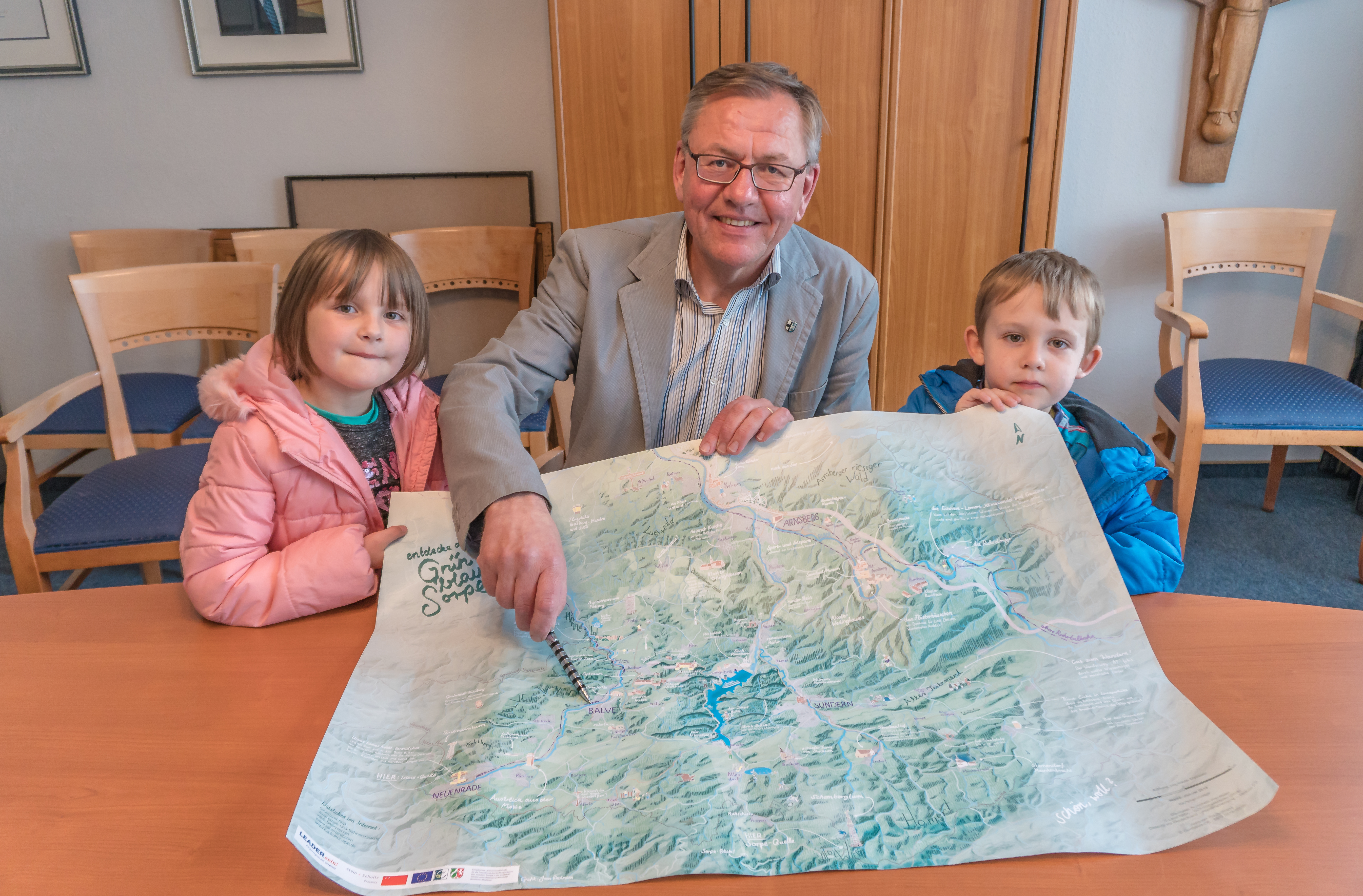 Michael Bathe, Allgemeiner Stellvertreter des Bürgermeisters, zeigt Johanna und Jonathan, wo sich die Stadt Balve auf der Karte befindet. In diesem Jahr können Vereine und Bürger insgesamt 5.000 Euro beim Heimat-Preis gewinnen. Foto: Sven Paul