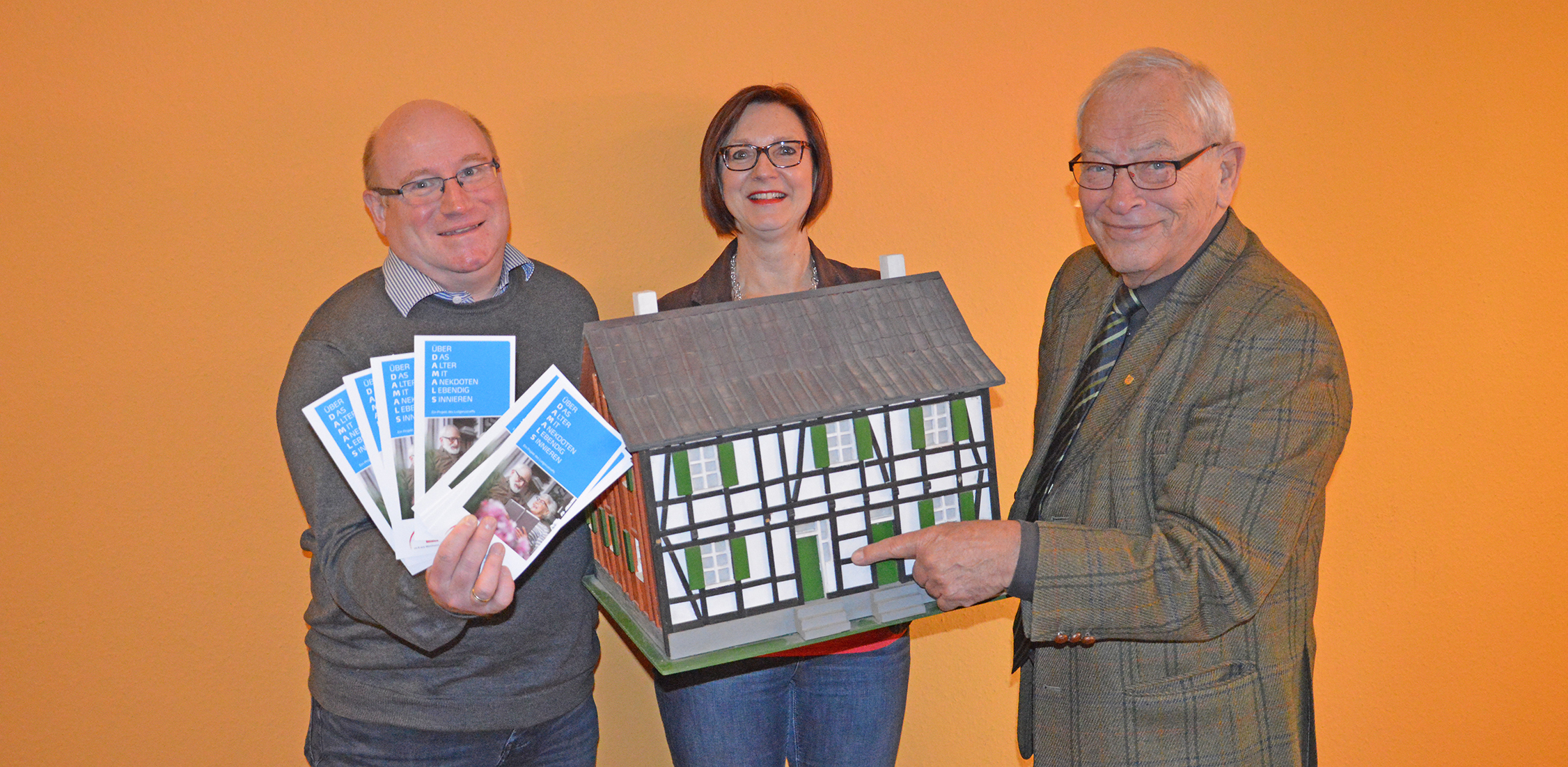 Peter Ihle (von rechts), ehemaliger Bürgermeister der Stadt Heiligenhaus, Ingrid Niering, Leiterin des Ludgerustreffs, und Martin Wildner, Abteilungsleiter der Sozialen Dienste für Senioren beim Caritasverband, stellten gemeinsam die Programmpunkte des Projektes "Über DAMALS" vor. Hier zu sehen sind sie mit einem Model des Bösenhauses, das einst auf der Hauptstraße in Höhe des Kirchplatzes stand.