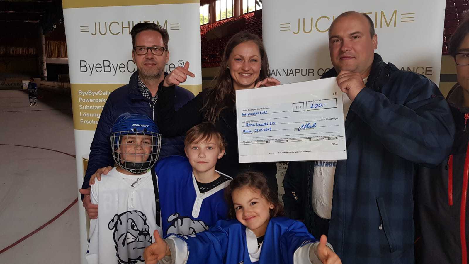 Rebeka Skurak und Michael Weber übergeben Sebastian Cirkel von UbE den Scheck. Die Scheck-Übergabe fand in der Eissporthalle Unna bei Dreharbeiten zu einem Werbefilm statt.