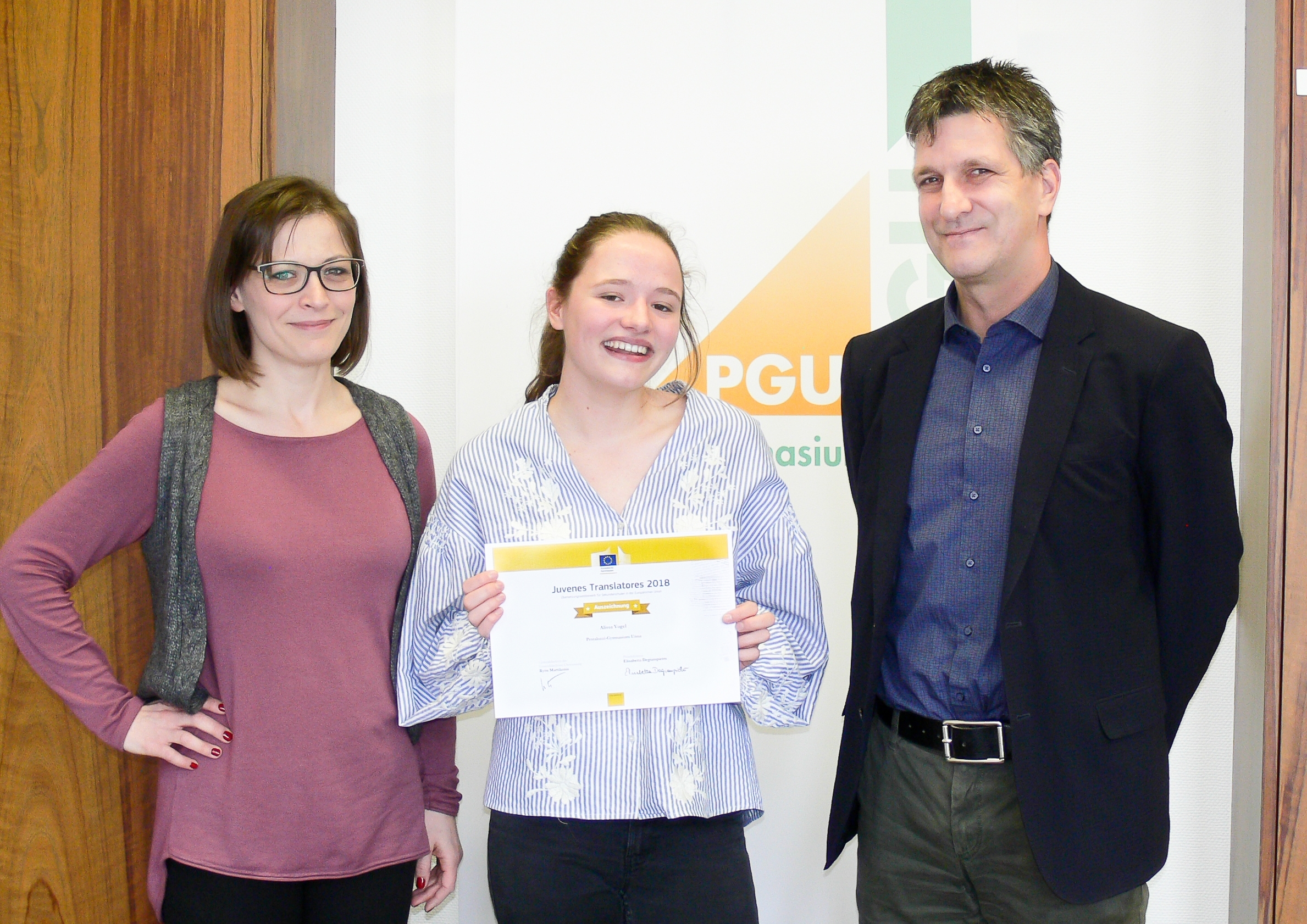 Stolz überreichen Schulleiter Dirk Kolar und Lehrerin Anna Brinkel (Koordinatorin des Übersetzungswettbewerbs am PGU) die Urkunde an Alissa Vogel (Q1).