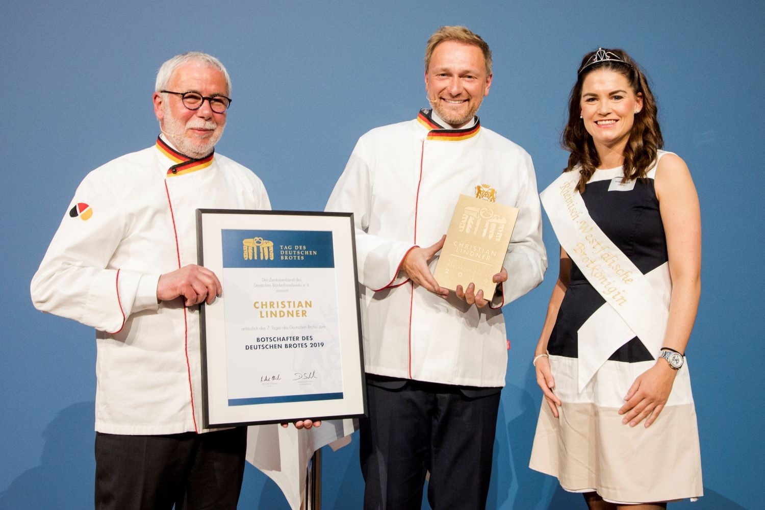Melissa Nietsch, amtierende Rheinisch-Westfälische Brotkönigin, assistiert Innungs-Präsident Michael Wippler (l.) und stattet den neuen Brotbotschafter Christian Lindner mit Jackett und Pokal aus. Foto: Deutsche Bäckerinnung e.V.