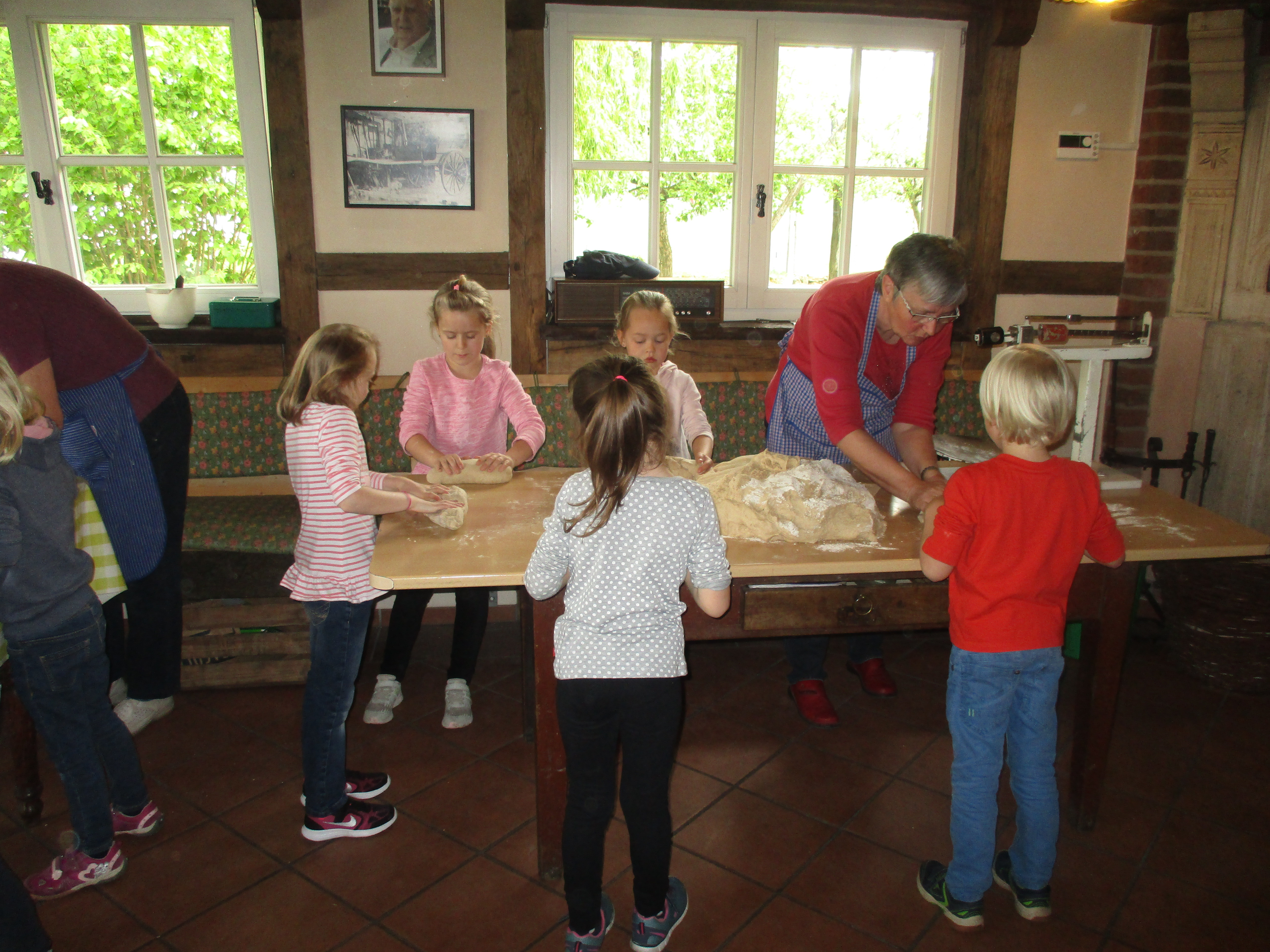 Irmgard Humme buk mit den Kindern und Eltern Brot im Backhaus und erklärt, wie Mehl und Zutaten geknetet und zu Brotlaiben geformt werden.