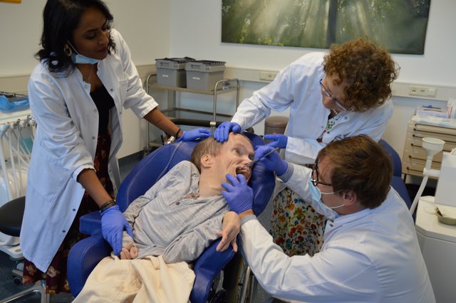 Patient Marco Schulle lässt sich von Dr. Peter Schmidt in den Mund schauen. Zahnärztin Dr. Gisela Goedicke-Padligur und der zahnmedizinischen Fachangestellten Ratheepana Thiagarajah unterstützen ihn.