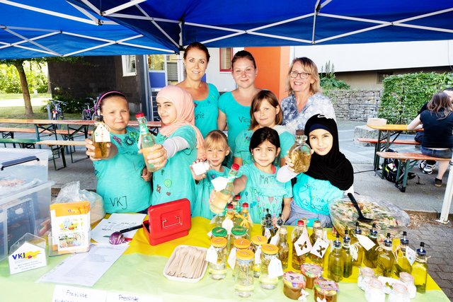 Köstliches aus eigenem Anbau: Zusammen mit VKJ-Erlebnisgarten-Projektleiterin Melanie Stroisch, VKJ-TalentKochtopf-Projektleiterin Victoria Behrendt und Monika Heyd, beim VKJ zuständig für die Bereiche Jugend und Kultur (v.l.), informierten Fatima, Seitab, Fiona, Lana, Loren und Emily die Besucher des Quartiersfestes über ihre Projekte und boten gleichzeitig die schmackhaften Ergebnisse aus Erlebnisgarten und TalentKochtopf an, zum Beispiel Kräuter-Öle, Kräuter-Salze und Marmeladen. Foto: VKJ/Lukas