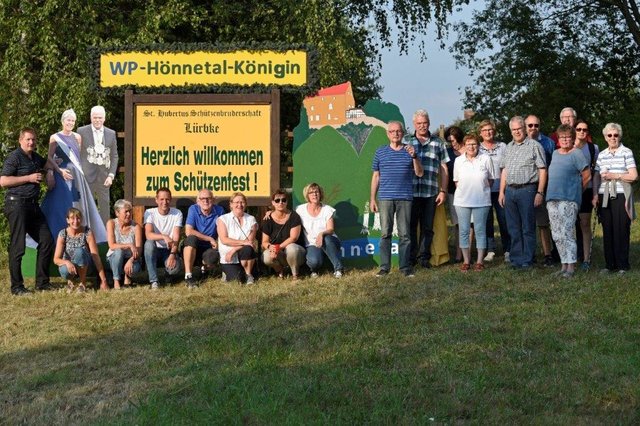 Königspaar mit Hofstaat und einige Vereinsmitglieder am Begrüßungsschild zum diesj. Lürbker Schützenfest vom 10. bis 12. August.